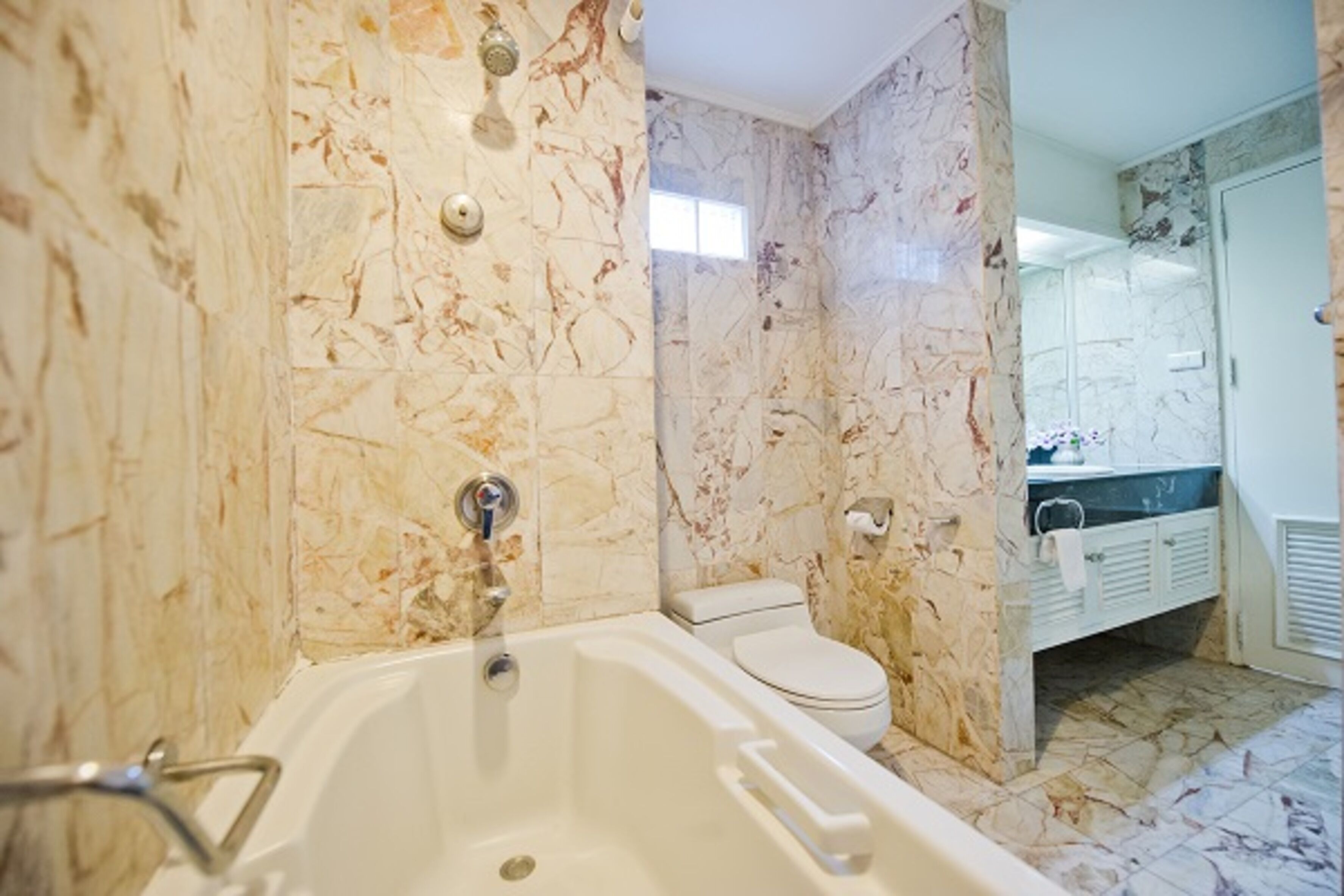 A bathroom with a marble wall, a bathtub, a toilet, and a sink with a mirror.