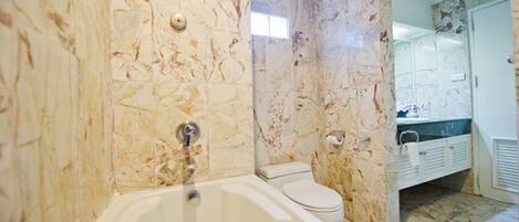 A bathroom with a marble wall, a bathtub, a toilet, and a sink with a mirror.