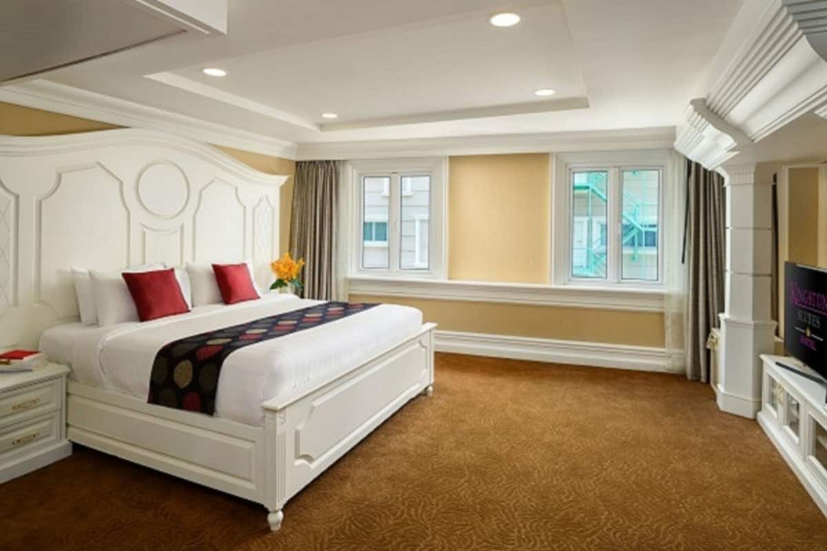 Une chambre d’hôtel avec un grand lit, une télévision, une fenêtre avec des rideaux et un sol recouvert de moquette.