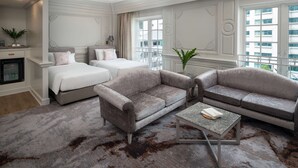 Een hotelkamer met een groot bed, twee banken, een bijzettafeltje en uitzicht op de stad door grote ramen.