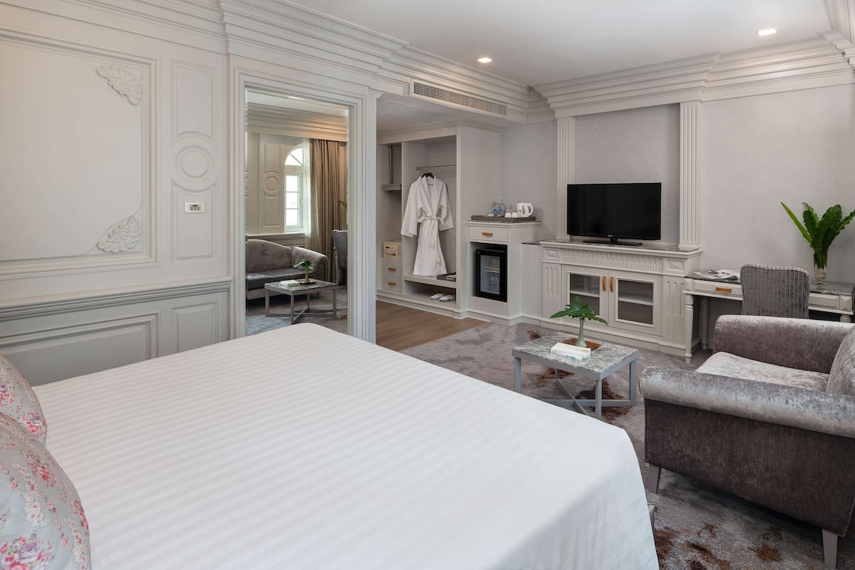 Une chambre d’hôtel dotée d’un grand lit, d’un coin salon avec un canapé et des fauteuils, d’une télévision et d’une petite table agrémentée d’une plante.
