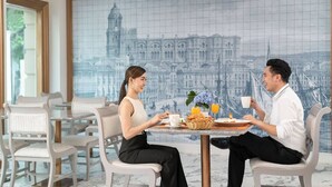 Een eetgedeelte met een tafel voor twee personen, met een stadsmuur, zachte zitplaatsen en een ontbijtbuffet.