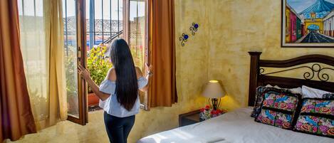 Una habitación con una cama, una ventana con cortinas, una lámpara y un cuadro en la pared.