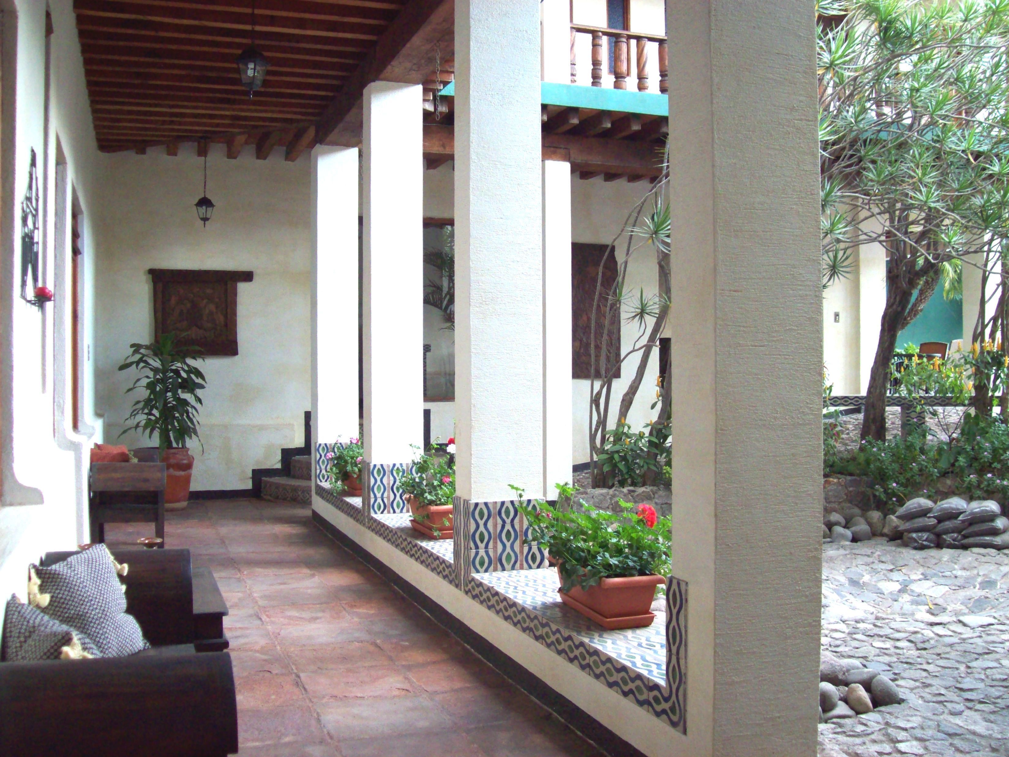 A covered patio area with a tiled floor, potted plants, and a seating area with a sofa and cushions.