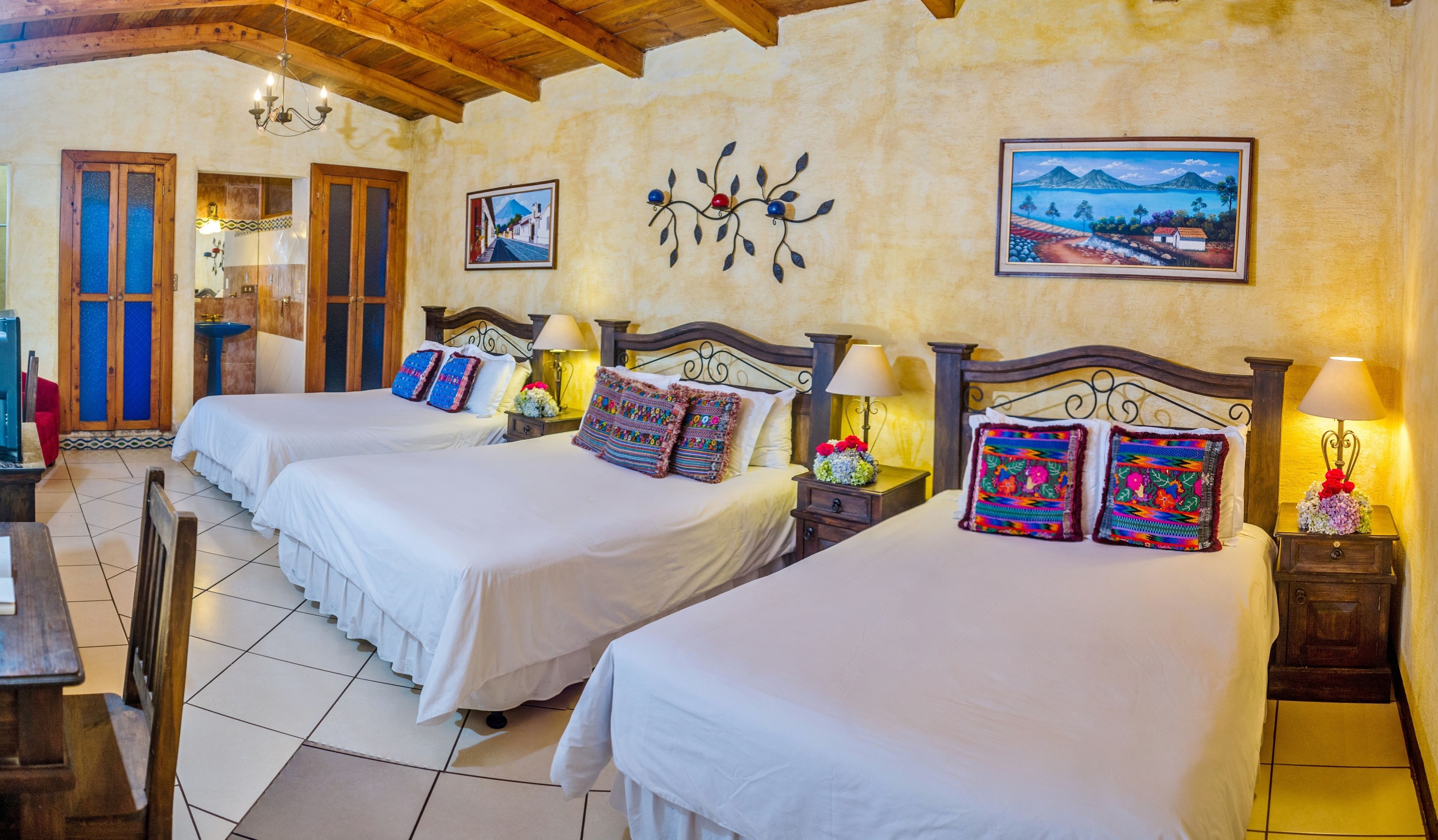 A hotel room with two beds, a wooden ceiling, a painting, and a view of the sea.