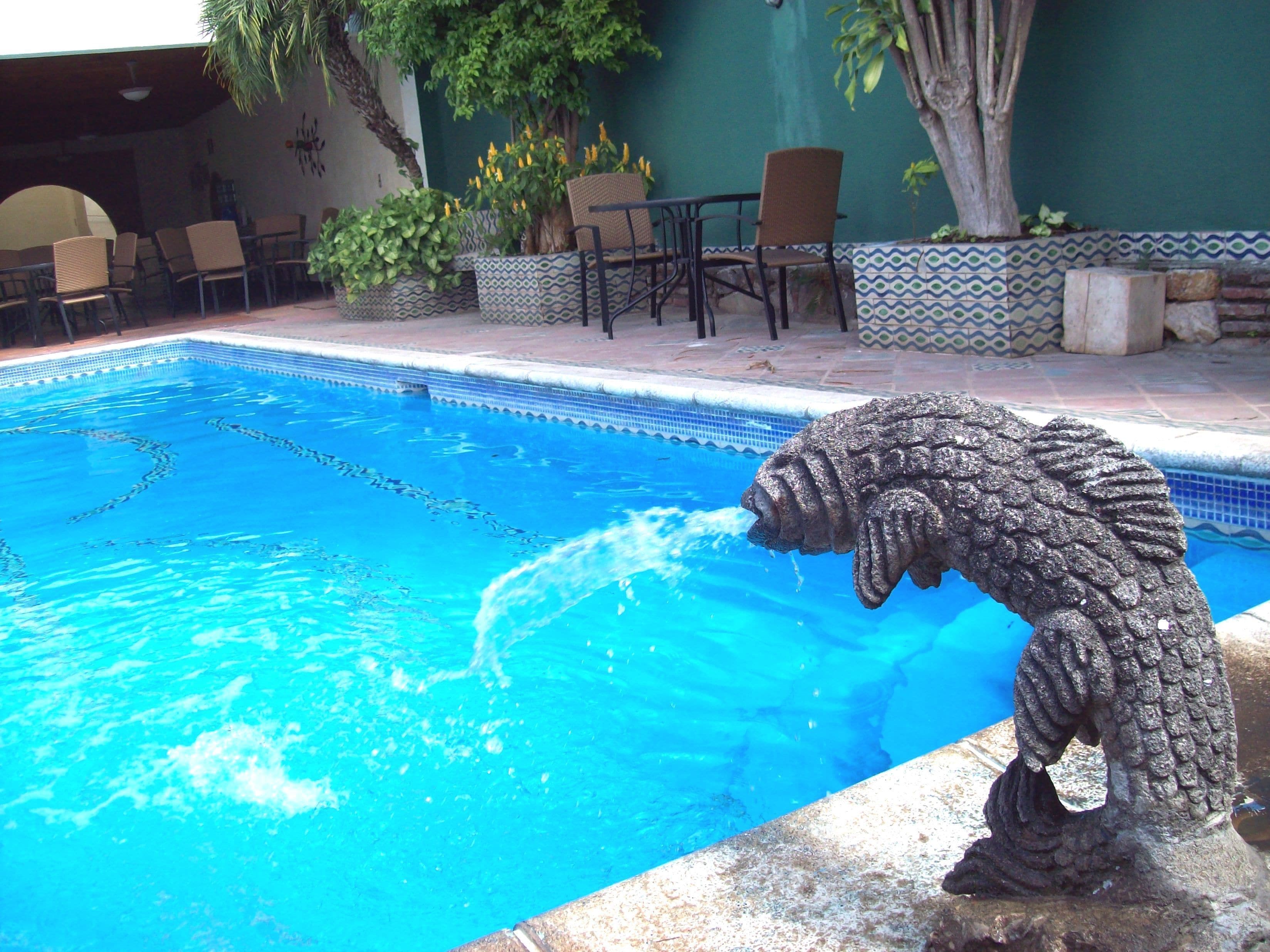 Una piscina amb una escultura de pedra, envoltada de cadires i plantes en testos.