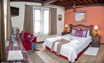 Una habitación de hotel con una cama, una silla roja, un escritorio con una computadora portátil, un televisor y una ventana con cortinas.