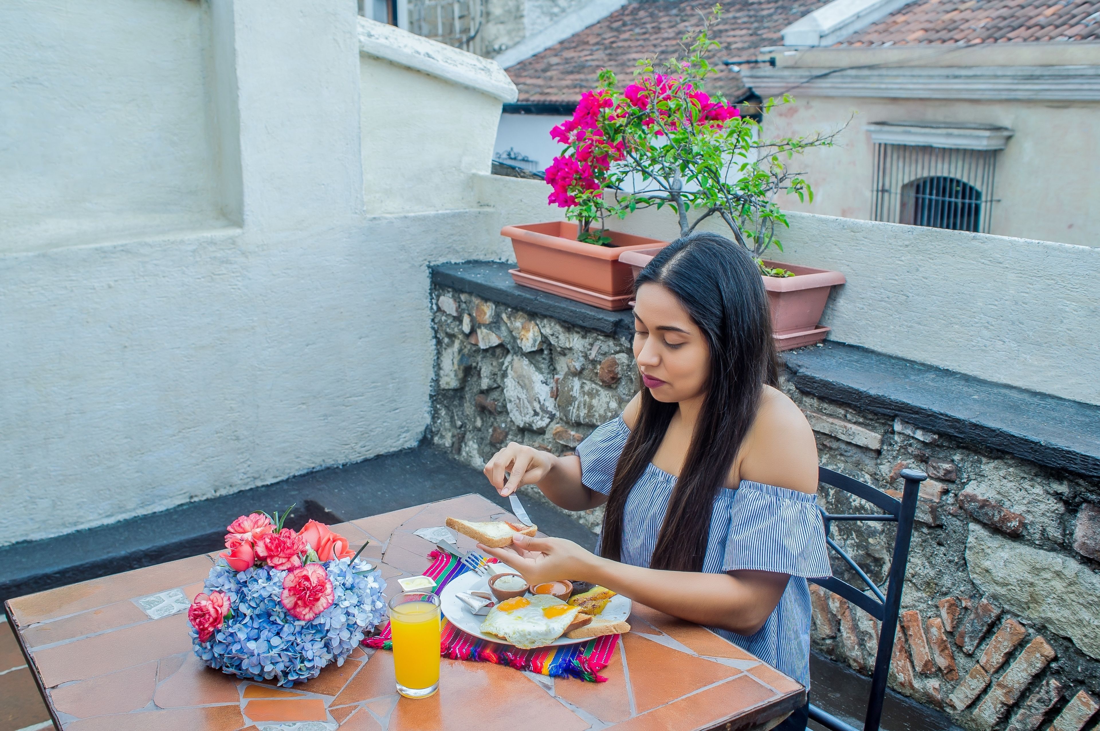 Une personne est assise à une table en plein air, devant un repas, une boisson et un arrangement floral.