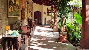 A sunlit corridor with rustic wooden beams, a stone floor, and potted plants. - Hotel Casa del Parque (Antigua Guatemala)