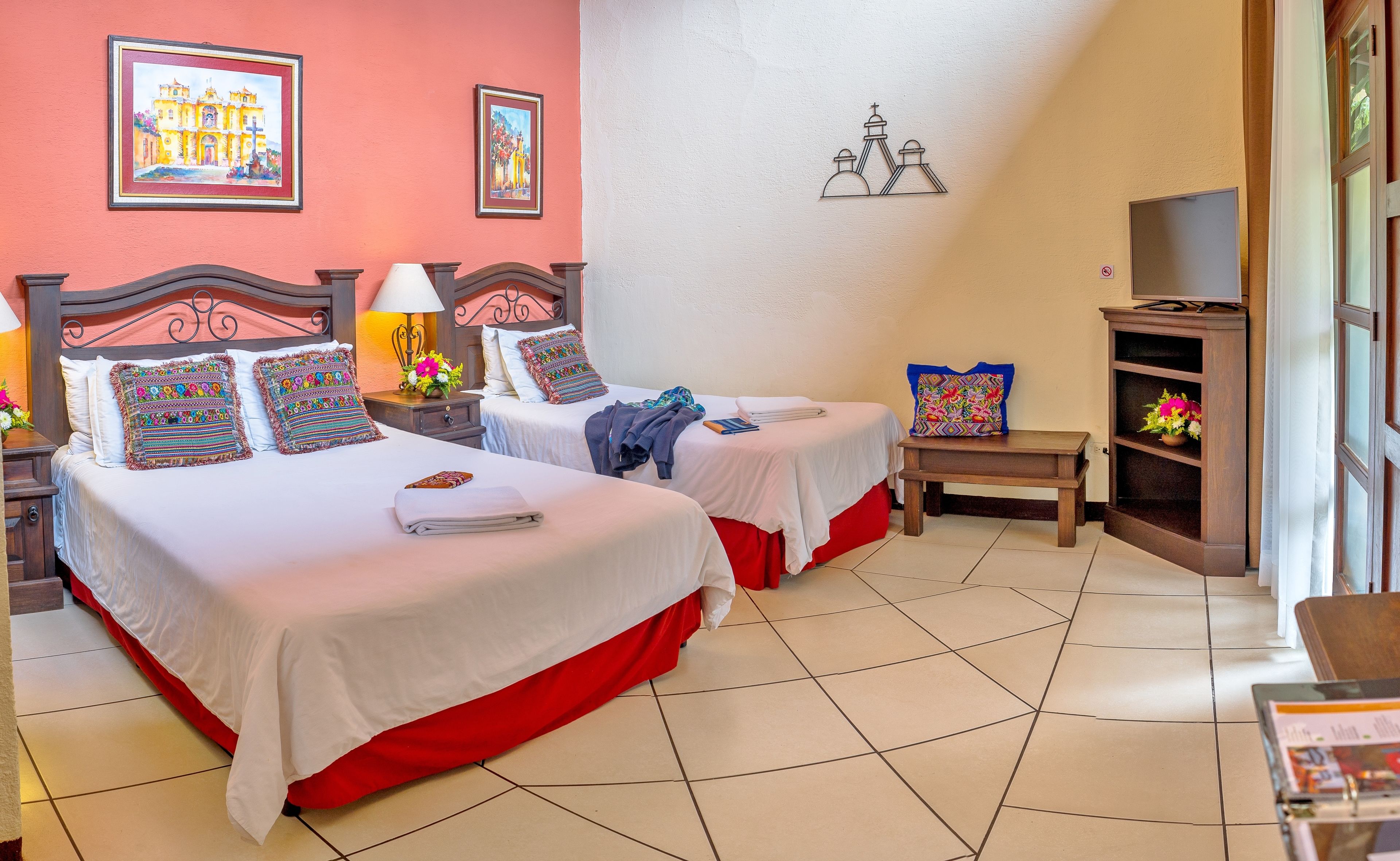 Een hotelkamer met twee bedden, een televisie, een klein tafeltje en een plank met bloemen.