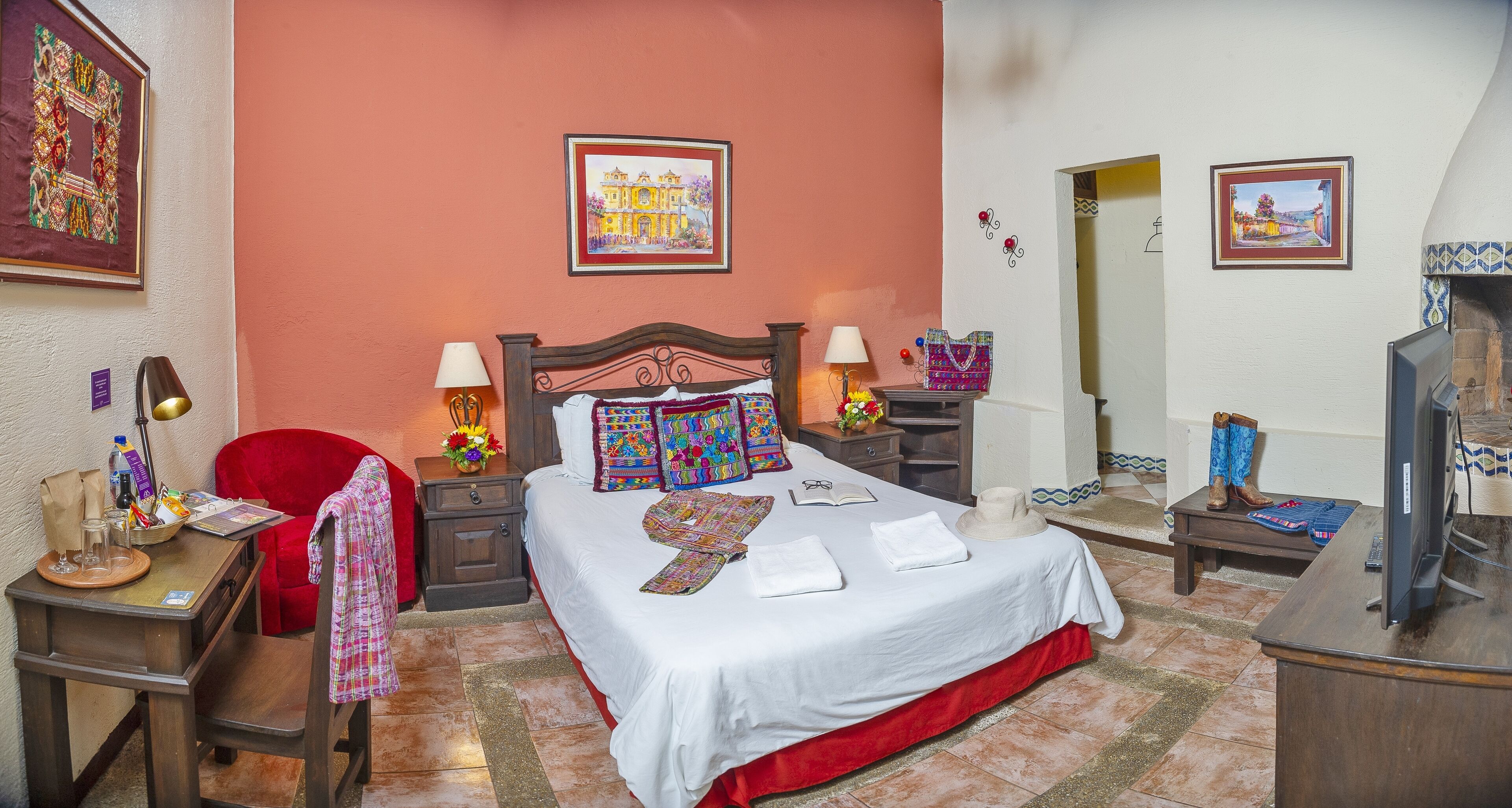 Een verzorgde hotelkamer met een bed, nachtkastjes, een rode stoel, een televisie en kunstwerken aan de muren.