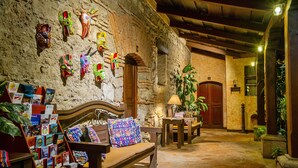 Un ambiente acogedor con pared de piedra, banca de madera y un rincón pequeño para leer, con libros y una lámpara.