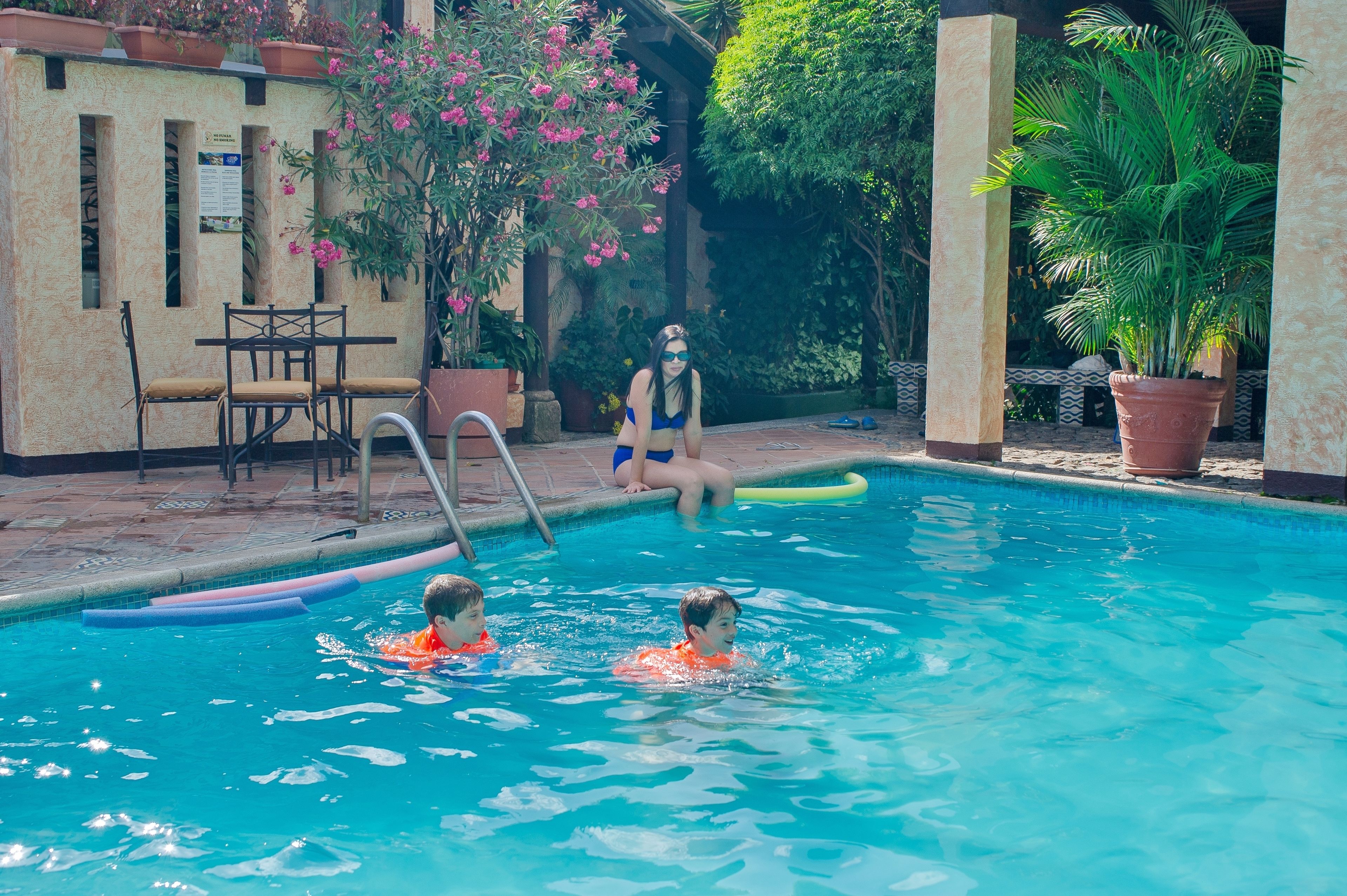A swimming pool area with a pool ladder, chairs, and potted plants.