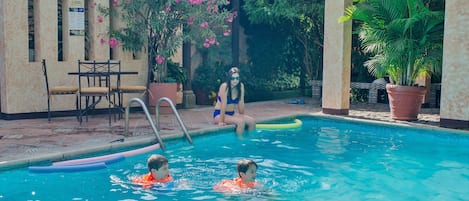 A swimming pool area with a pool ladder, chairs, and potted plants.