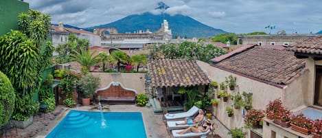 A pool area with lounge chairs, a fountain, and a view of a mountain.