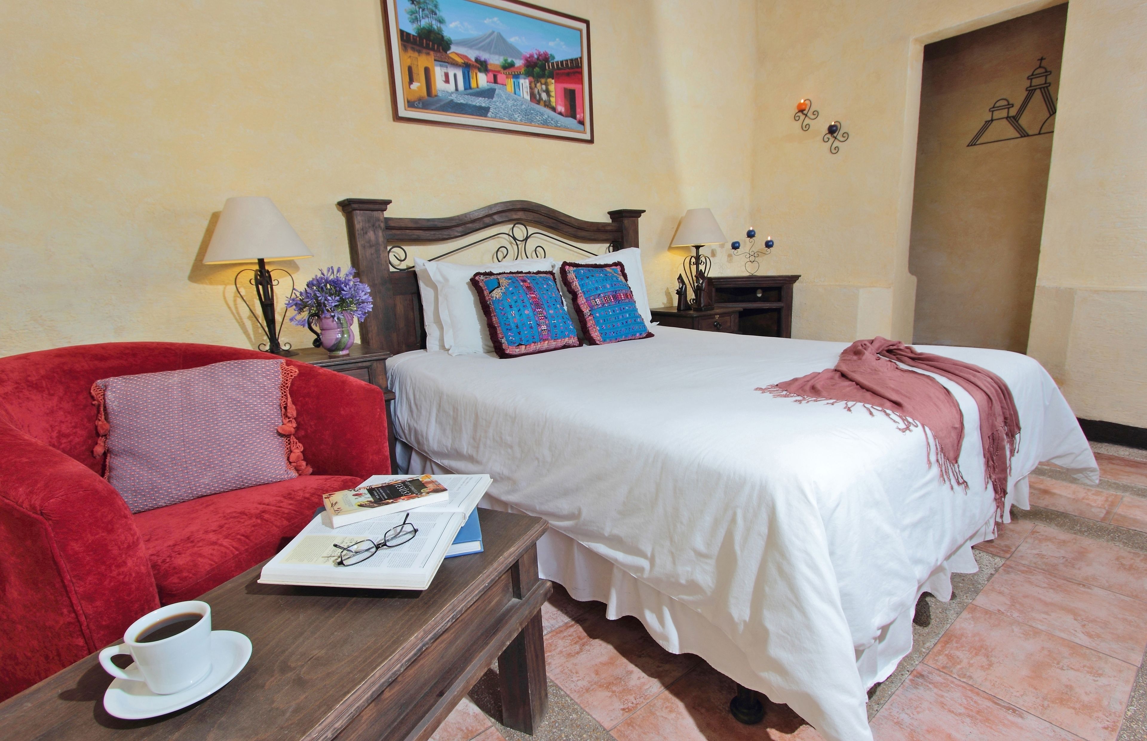 A hotel room with a bed, a red sofa, a coffee table, and a painting on the wall.
