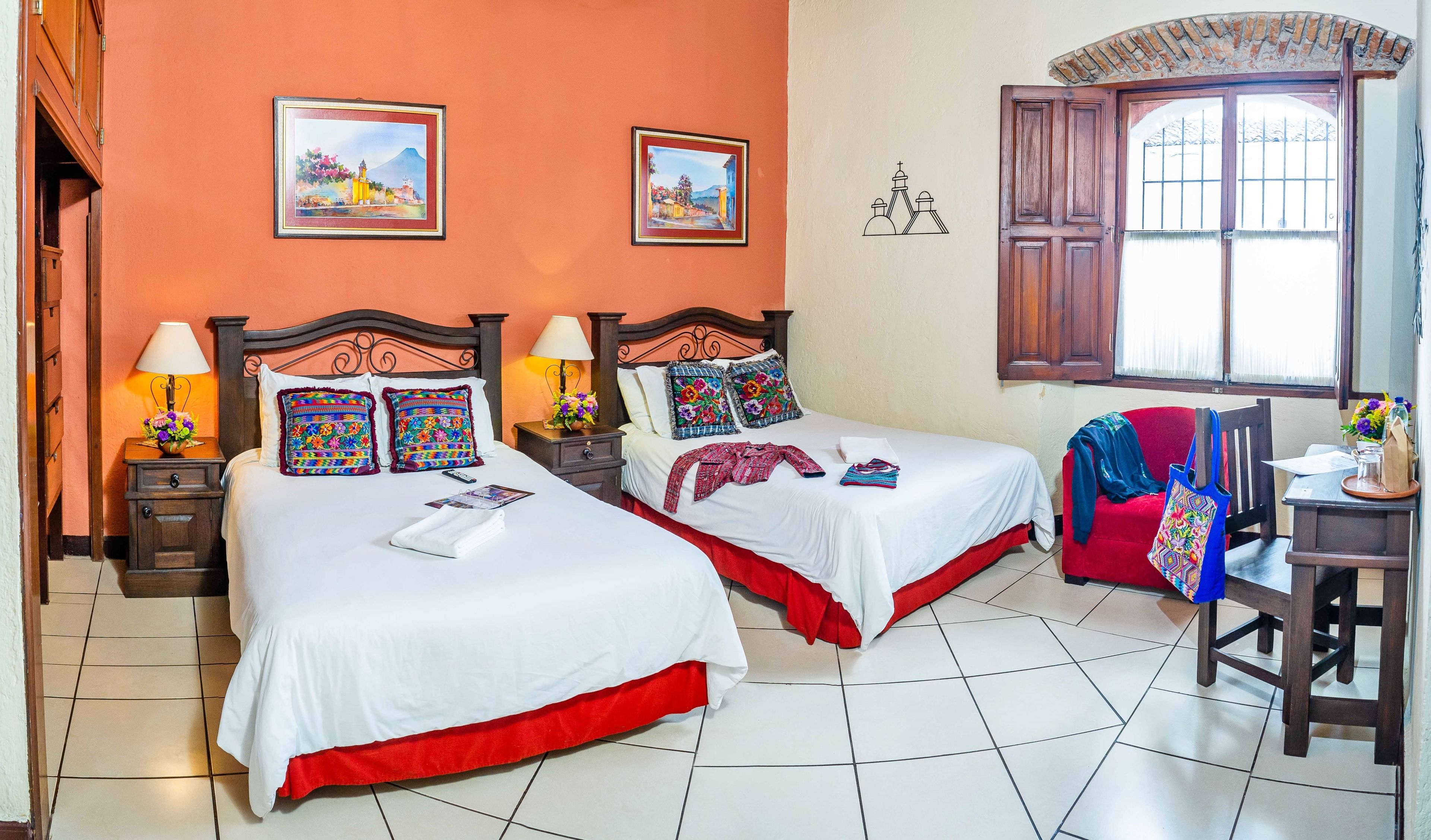 Une chambre d’hôtel avec deux lits, une chaise rouge, une table en bois et une fenêtre donnant sur une montagne.