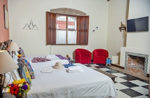 A hotel room with a bed, a window with curtains, a fireplace, and a checkered floor.