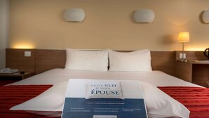 A hotel room with a neatly made bed, a bedside table with a lamp, and a brochure on the bed. - Kyriad ECO - Perpignan Nord Aéroport (Rivesaltes)