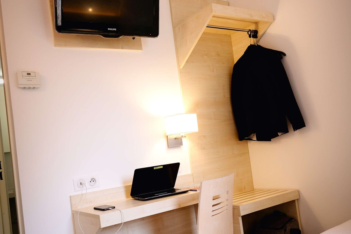 A hotel room with a flat-screen TV mounted on the wall, a desk with a laptop, a chair, and a bed.
