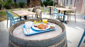 A wooden barrel table with a breakfast tray containing croissants, a cup of coffee, a glass of orange juice, and a small container of yogurt. - Kyriad ECO - Perpignan Nord Aéroport (Rivesaltes)