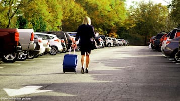 A parking lot with rows of parked cars and a person walking with a suitcase.