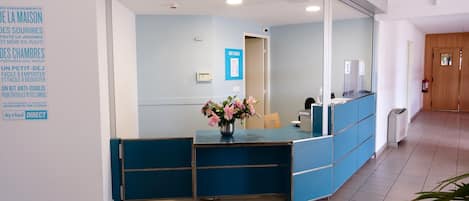 A reception area with a blue counter, a flower vase, and a sign indicating 'NOS TARIFS'.