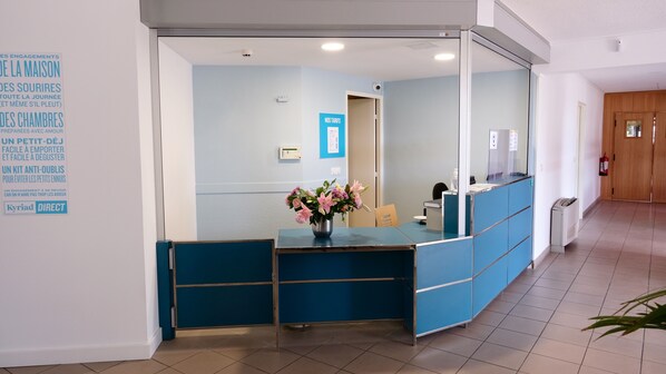 A reception area with a blue counter, a flower vase, and a sign indicating 'NOS TARIFS'. - Kyriad ECO - Perpignan Nord Aéroport (Rivesaltes)