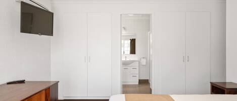A hotel room with a bed, a wooden dresser, a TV mounted on the wall, and a wardrobe.