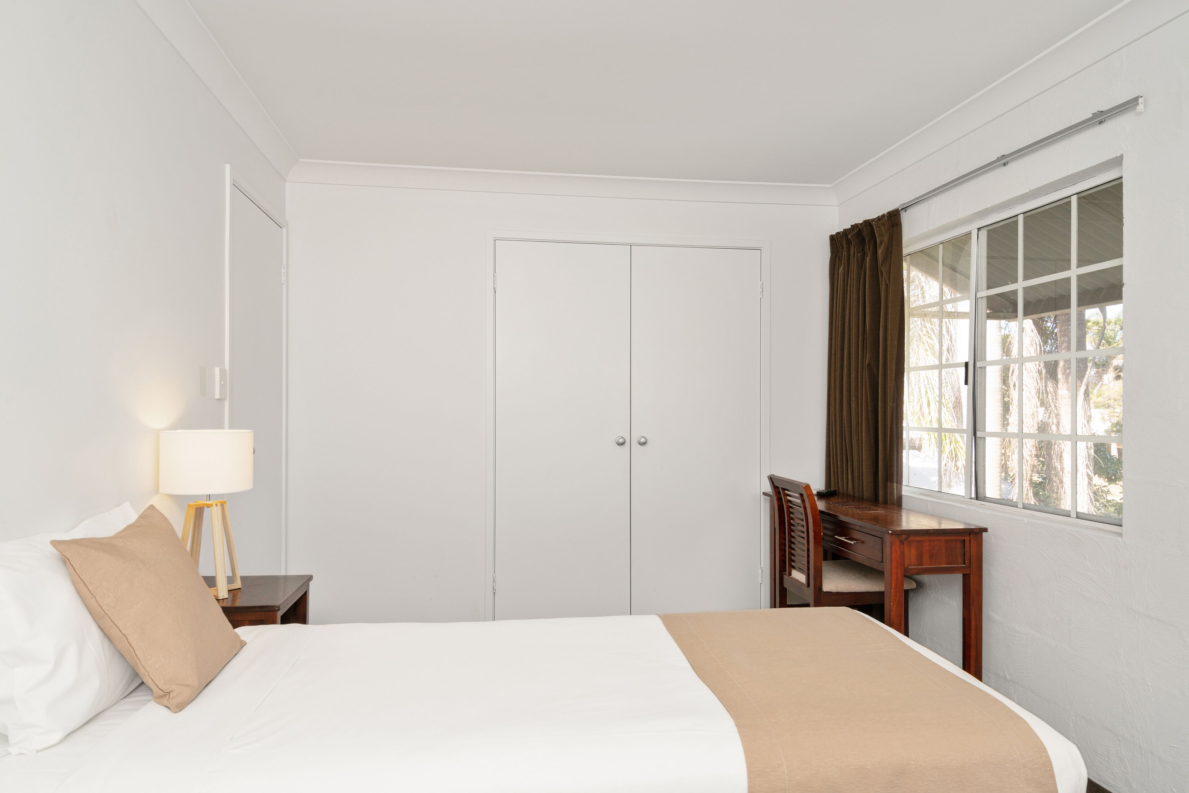 A hotel room with a bed, a desk, and a window with curtains.