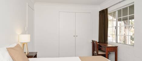 A hotel room with a bed, a desk, and a window with curtains.