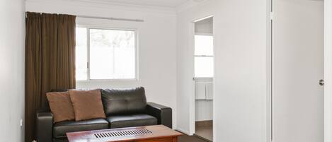 Ein modernes Wohnzimmer mit einem schwarzen Ledersofa, einem Holztisch und einem Deckenventilator.
