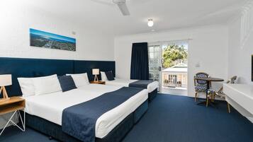 A hotel room with two beds, a desk, a chair, a balcony, and a ceiling fan.