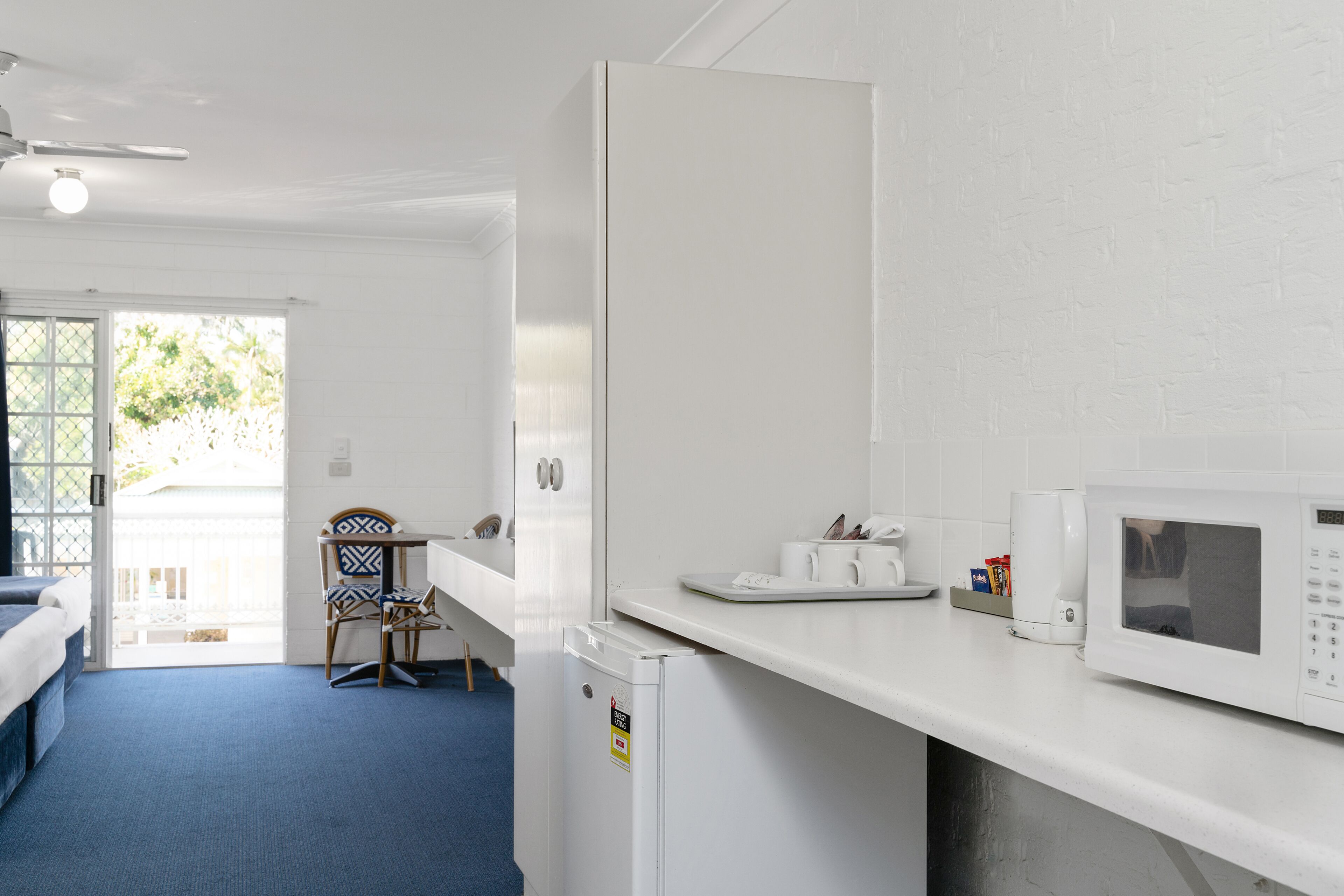 Habitación de hotel compacta con kitchenette, una cama, una silla y vistas al exterior.