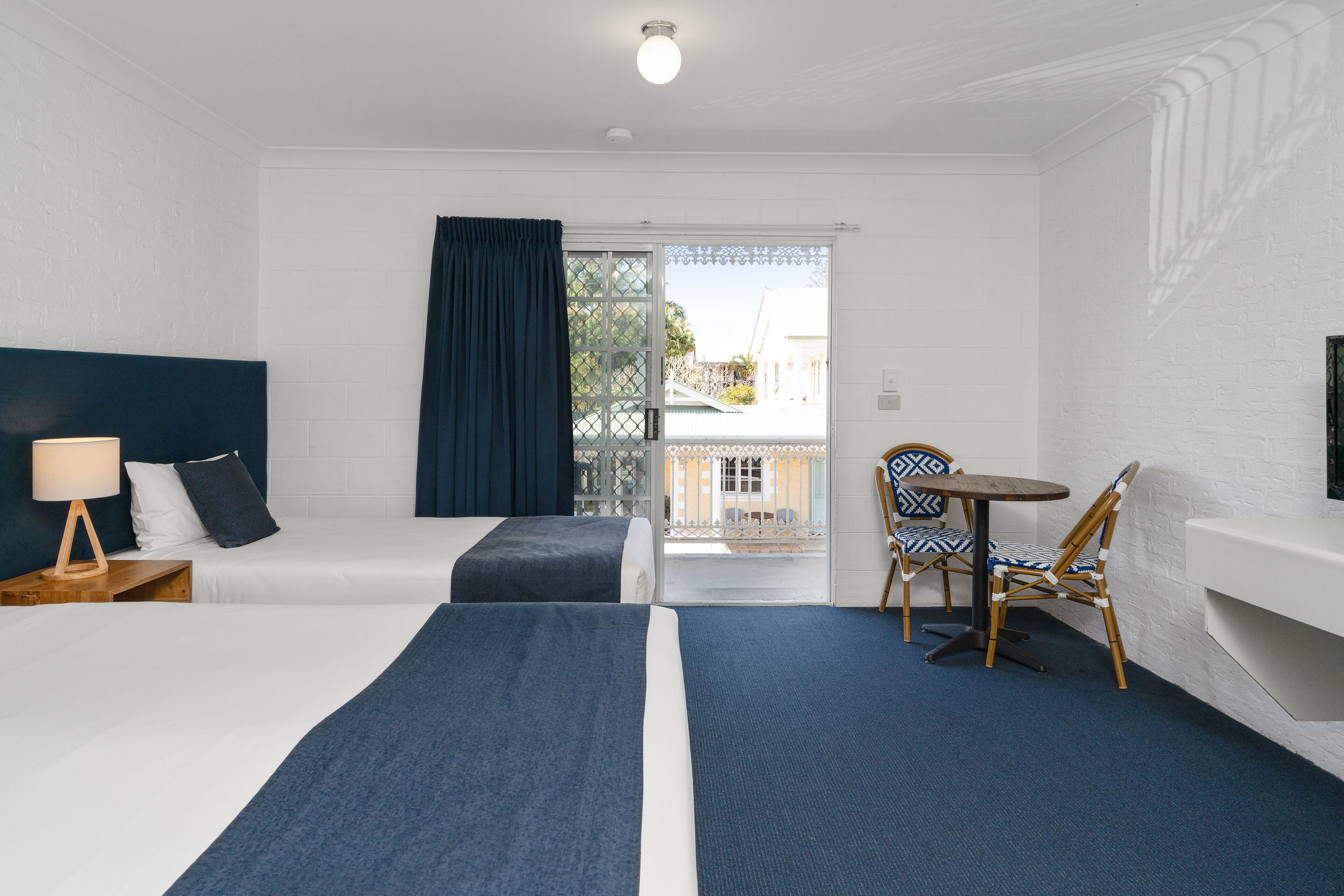 A hotel room with two beds, a small table with chairs, a TV, and a balcony with a view.