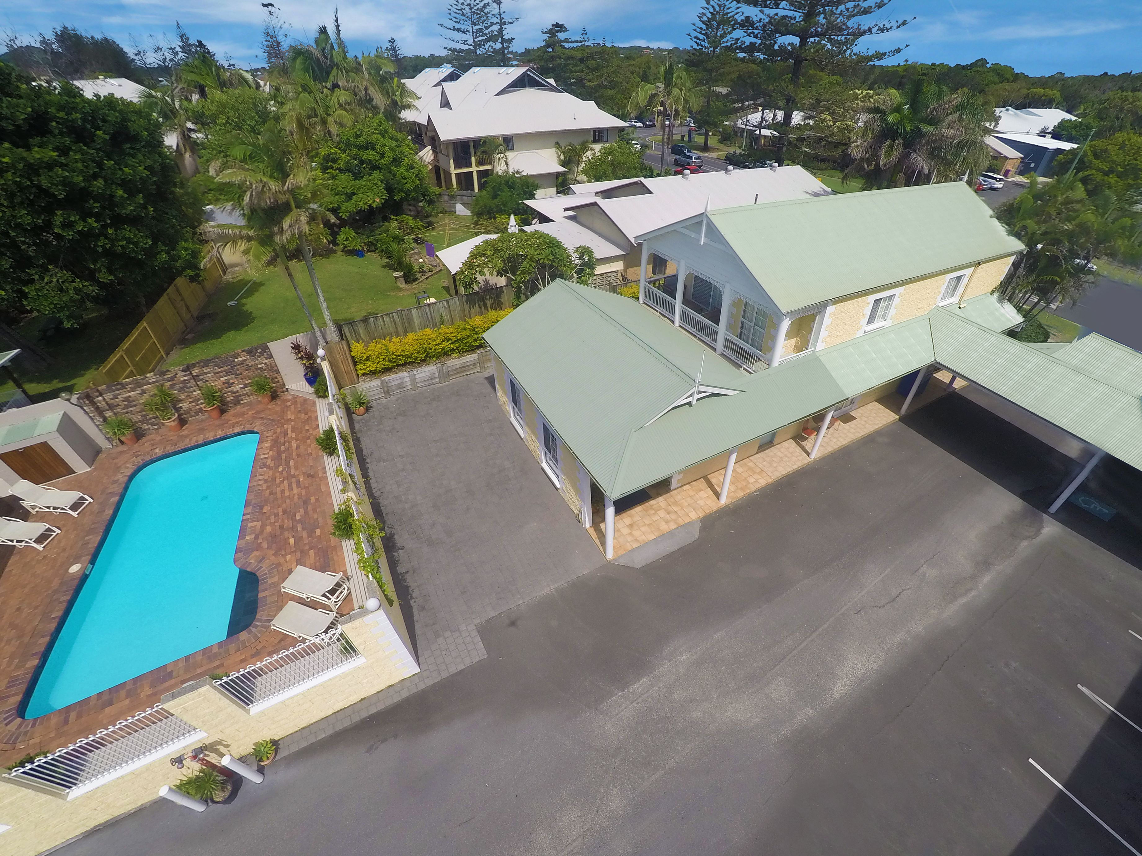 A residential area with a swimming pool, a covered patio, and a large house with a green roof.