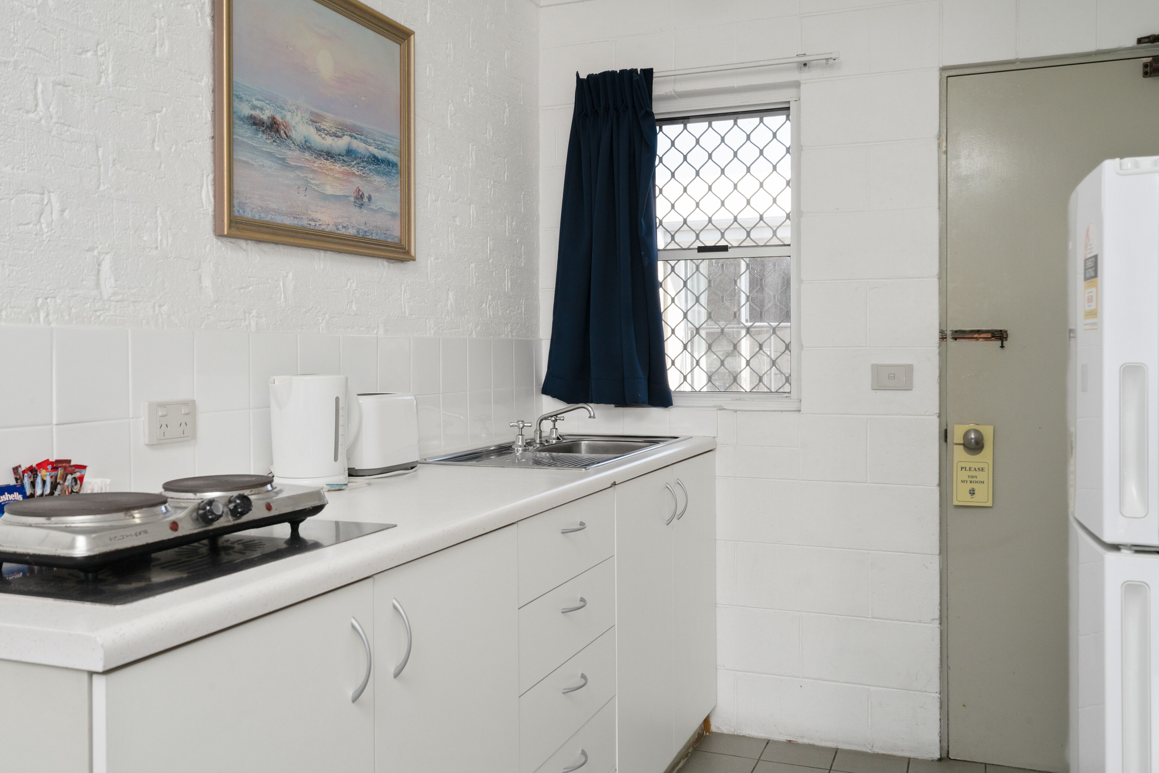 A kitchen with white cabinets, a stove, a sink, and a window with a blue curtain.