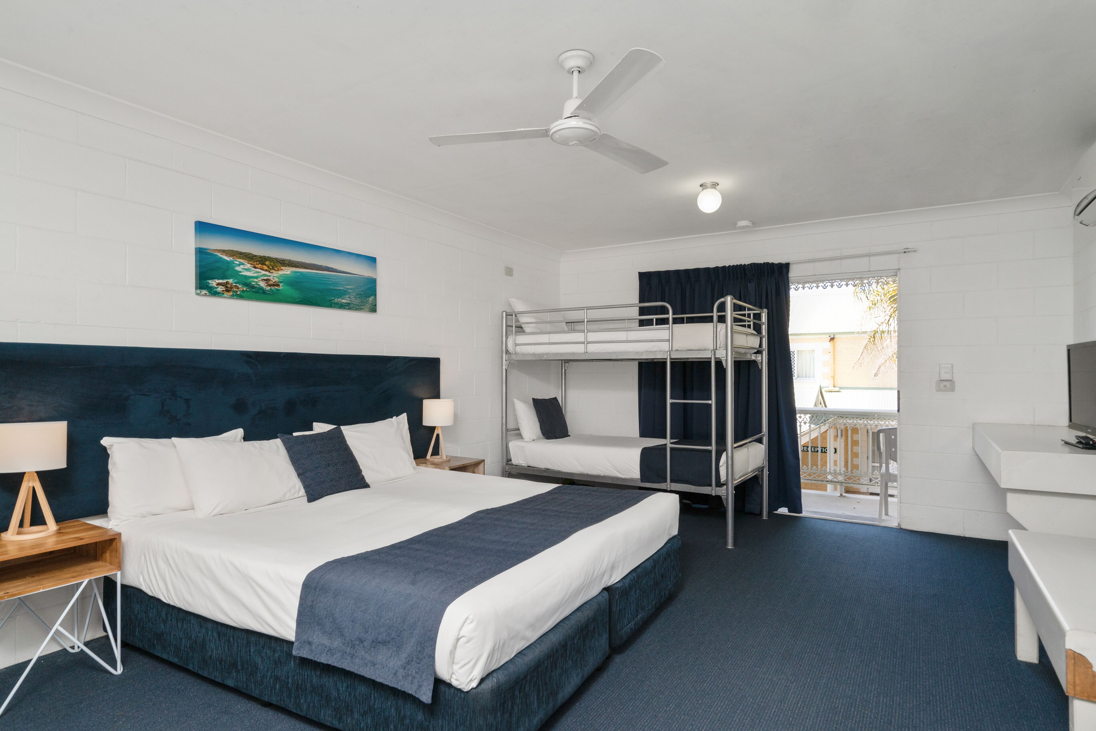 Ein Hotelzimmer mit Etagenbett, Schreibtisch, Stuhl, Deckenventilator und einem Bild an der Wand.
