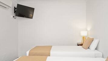 Habitación de hotel con dos camas, un televisor de pantalla plana montado en la pared, una mesita de noche con lámpara y aire acondicionado también instalado en la pared.