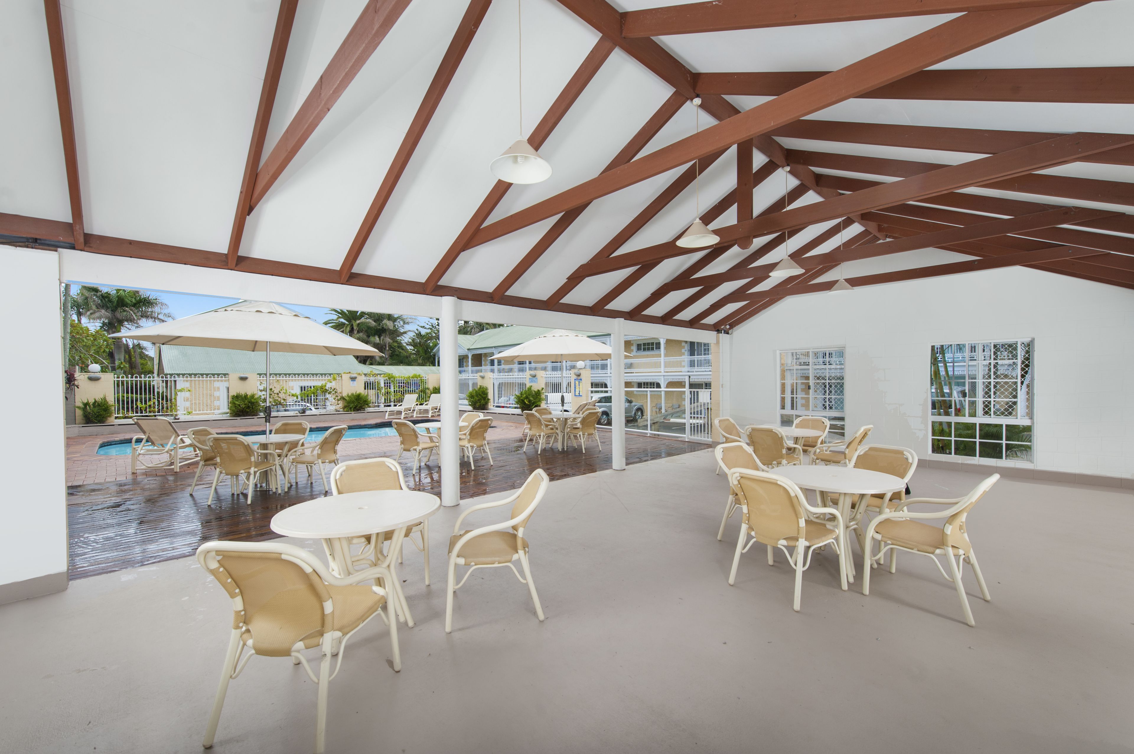 Un espacio al aire libre cubierto con mesas, sillas, una piscina y sombrillas.