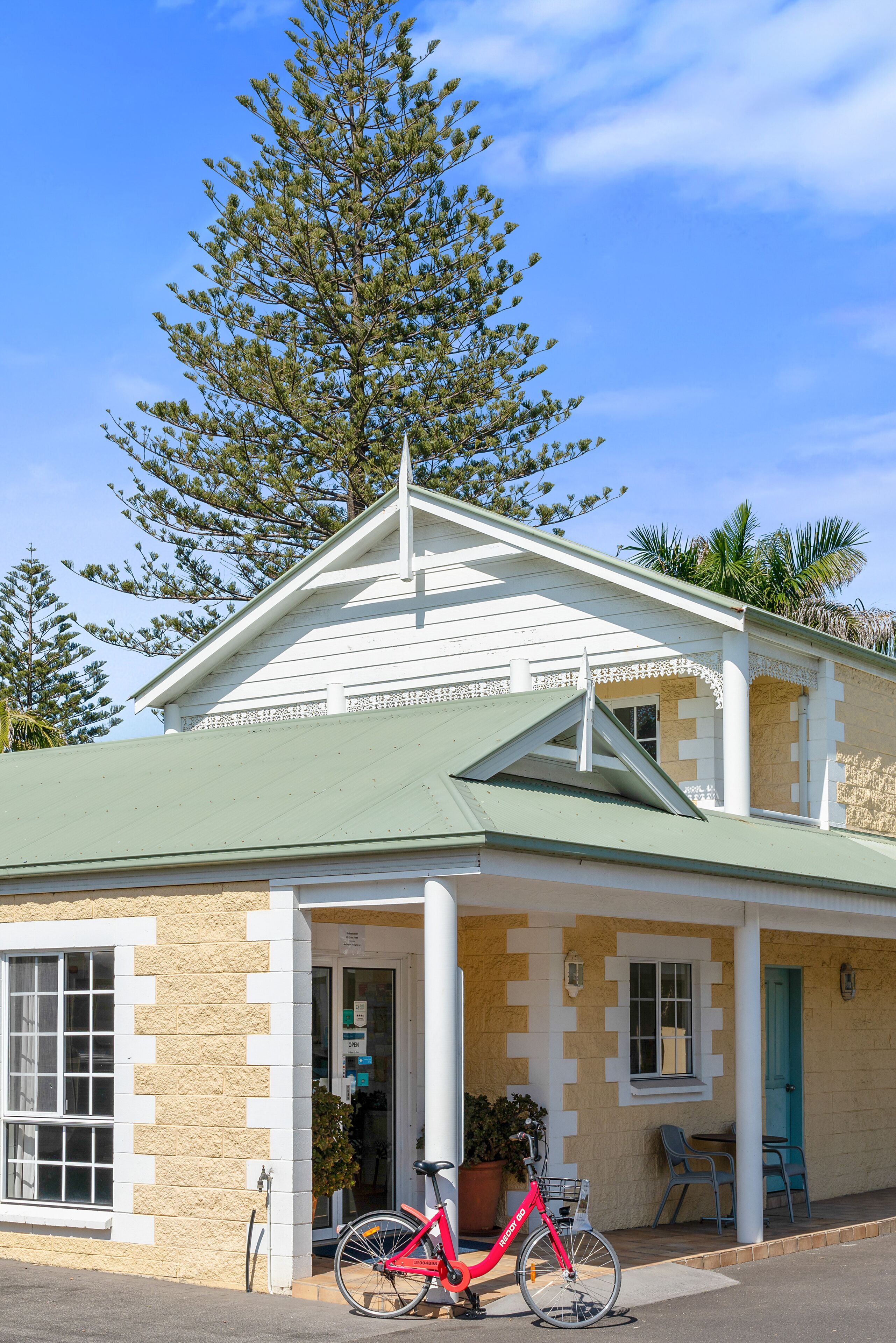 A building with a green roof, white trim, and a large tree in front.