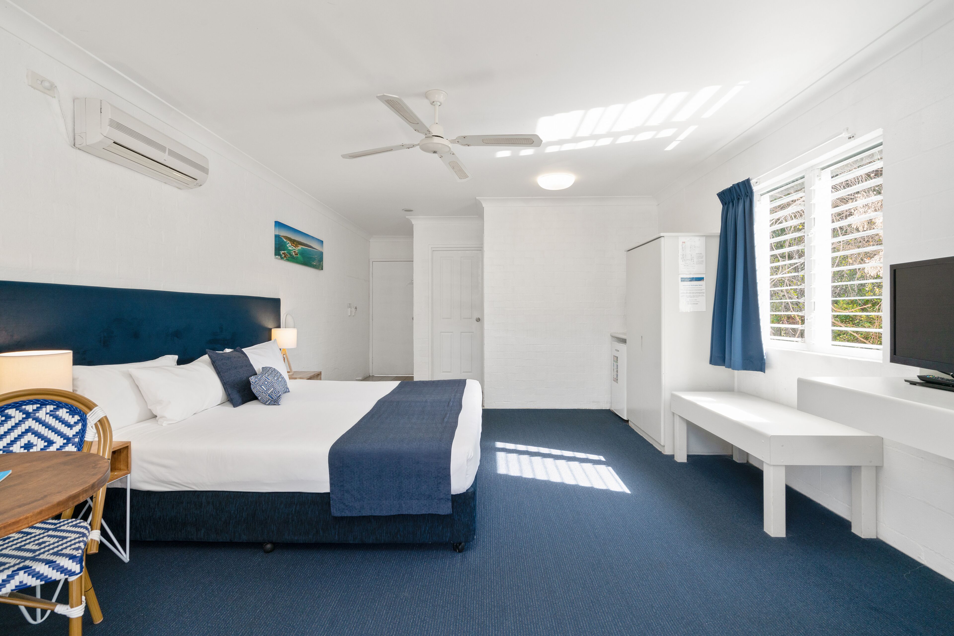 A hotel room with a bed, desk, chair, and a television.