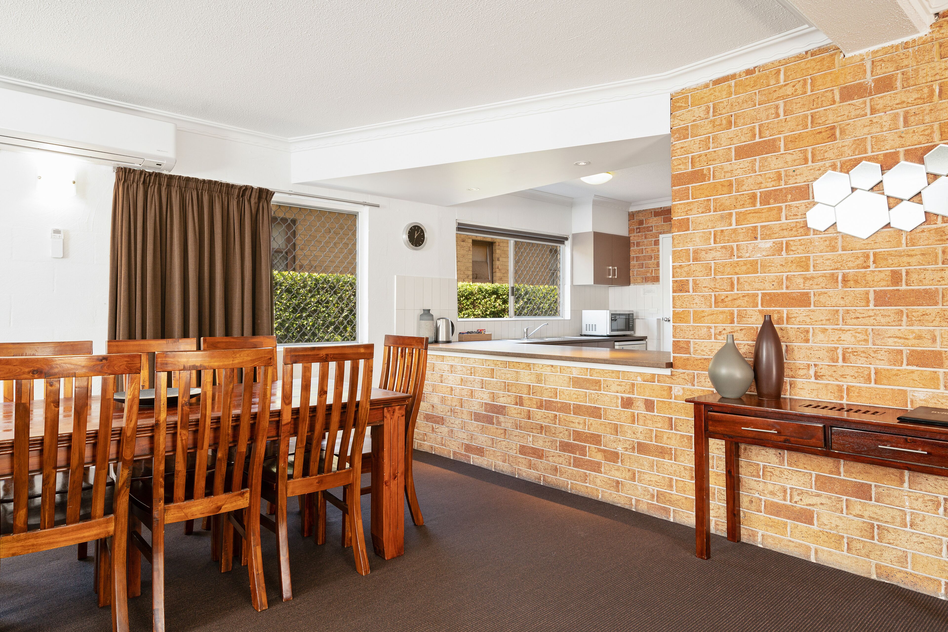 A modern kitchen with a brick wall, wooden dining table, and chairs.