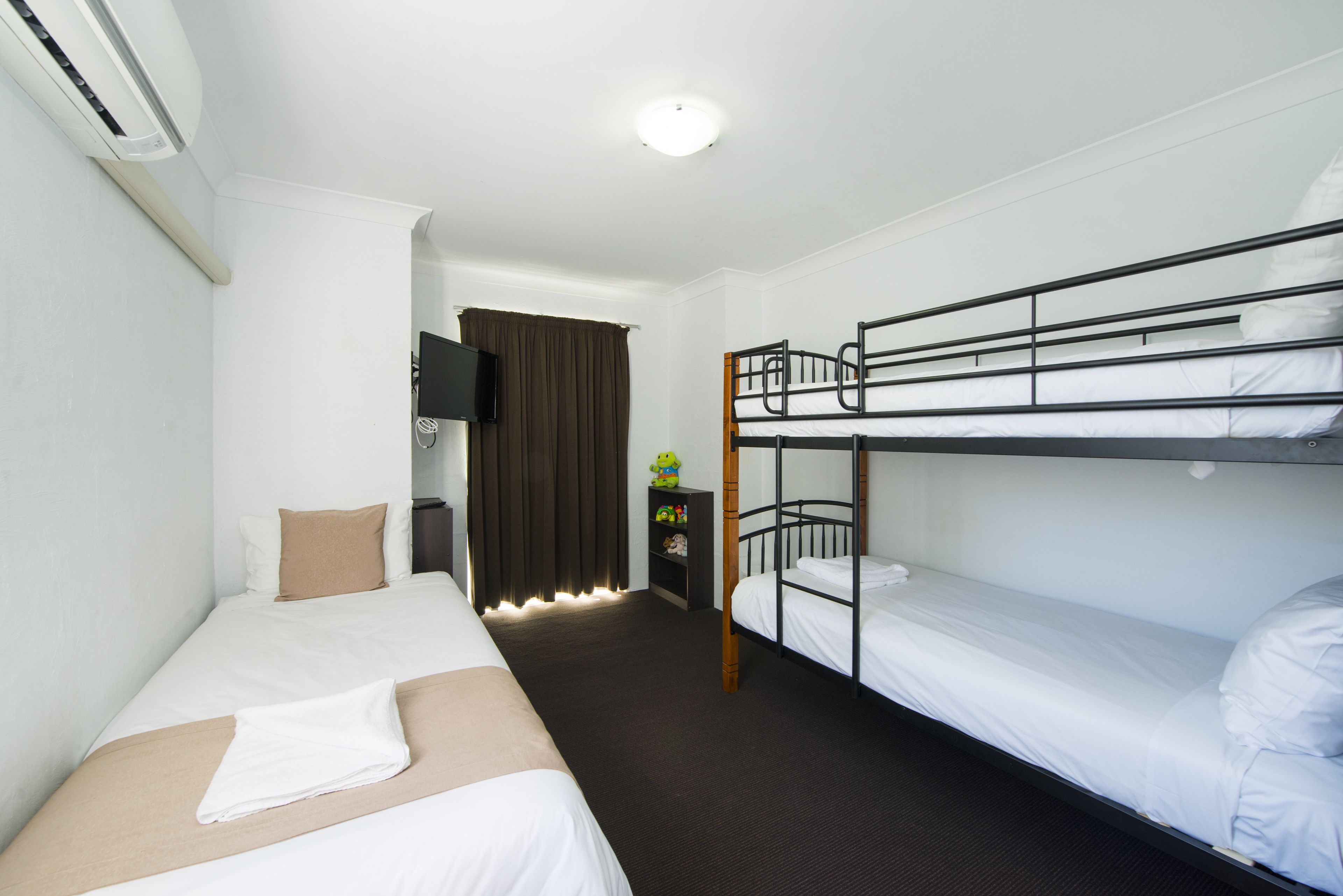 Habitación de hotel con literas, una cama individual, un escritorio con silla y televisor.