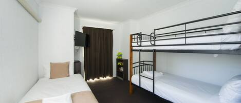A hotel room with a bunk bed, a single bed, a desk with a chair, and a television.