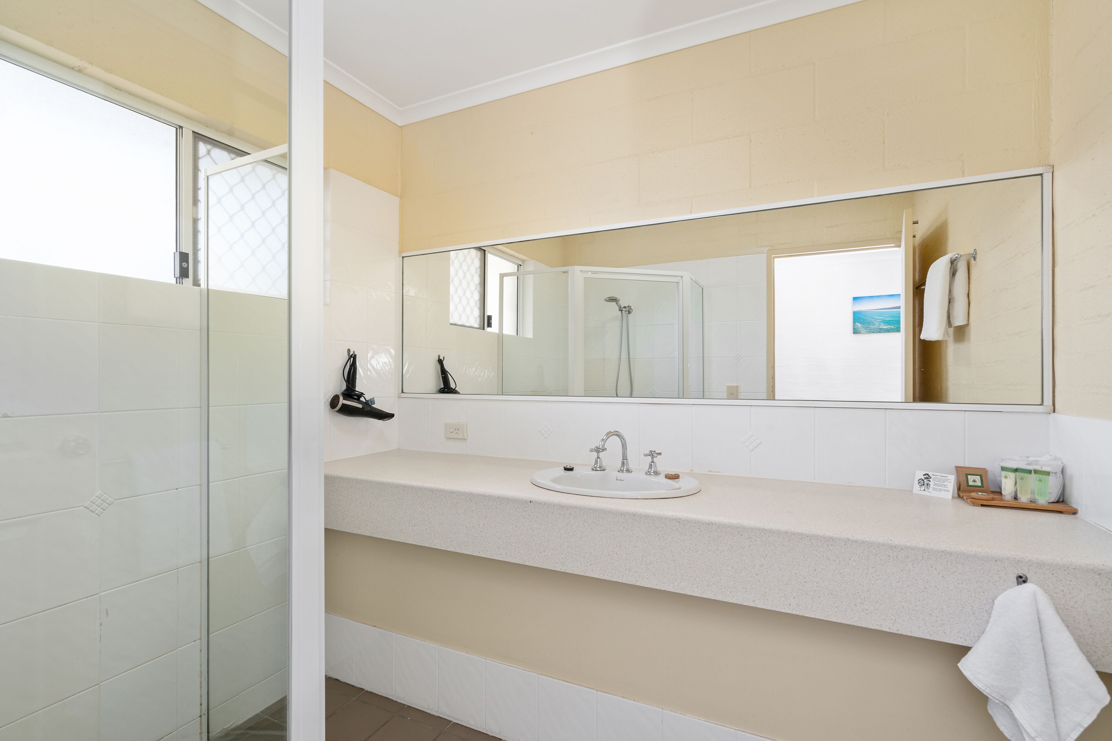 Un bagno con cabina doccia in vetro, uno specchio grande, un lavandino con rubinetto e un asciugamano appeso al muro.