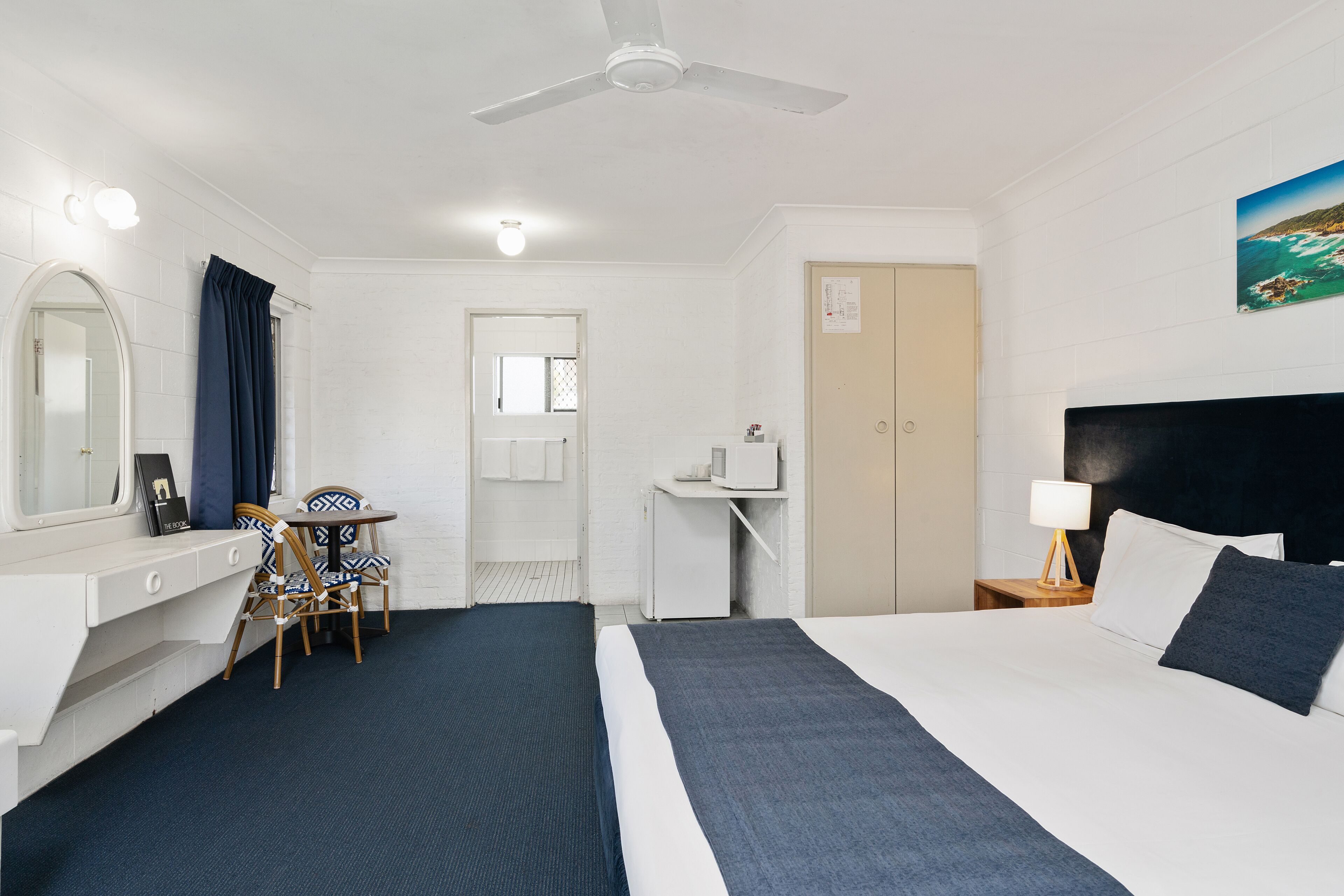 A hotel room with a bed, desk, chair, and a ceiling fan.