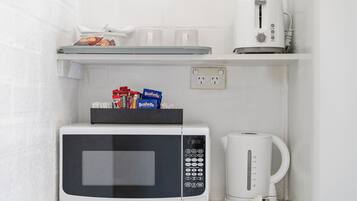 A compact kitchenette with a microwave, coffee maker, and a shelf with cups and snacks.