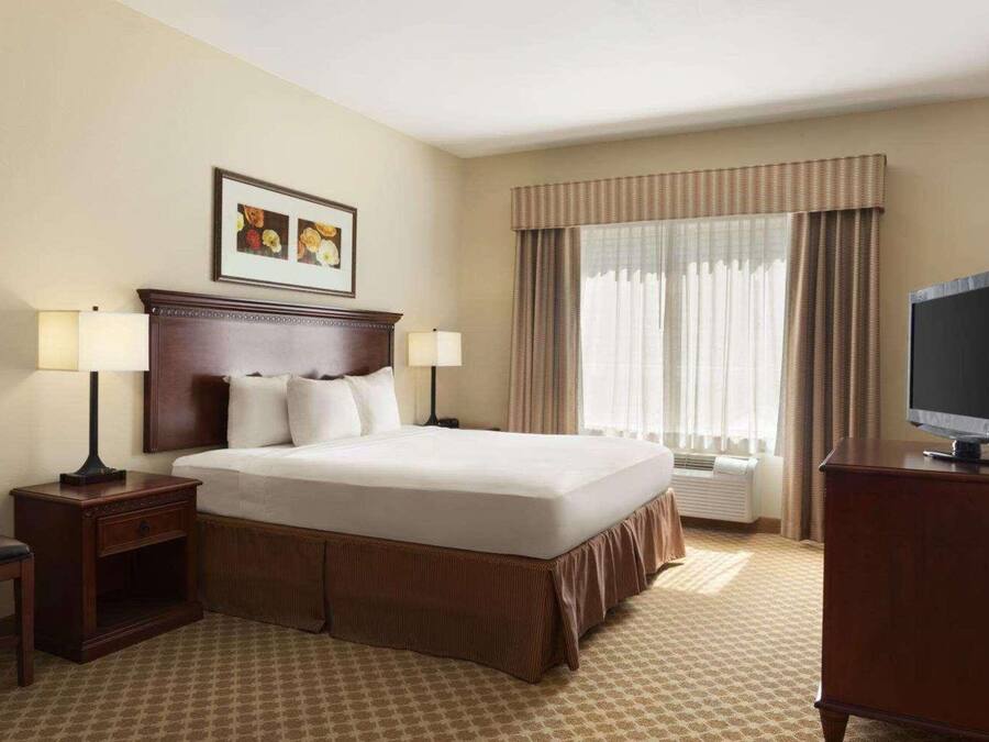 A hotel room with a large bed, two bedside tables with lamps, a television, and a window with curtains.