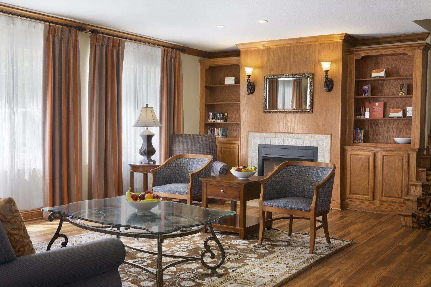 A living room with a glass-top coffee table, two upholstered chairs, a fireplace, and a bookshelf.